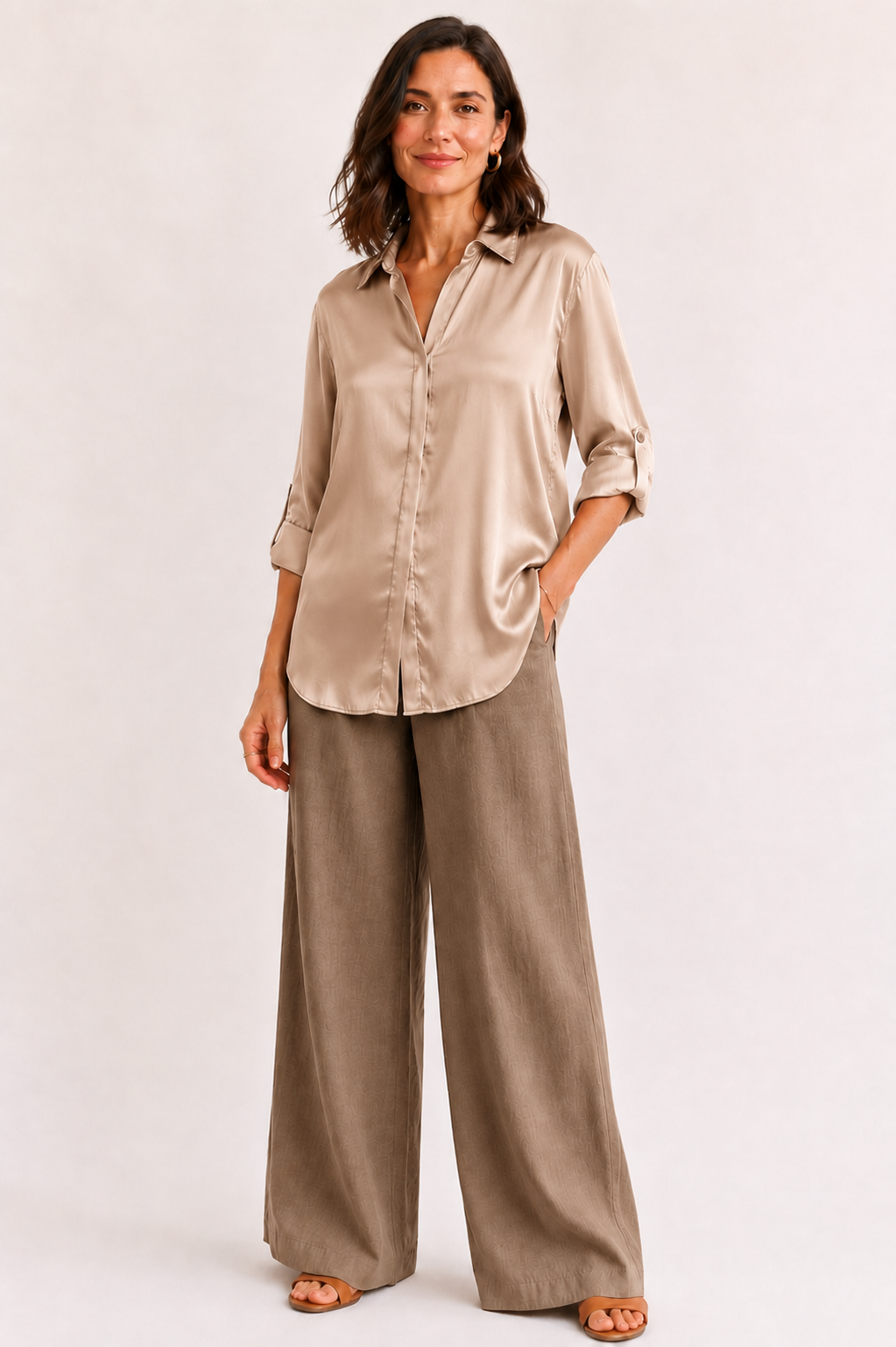 Woman wearing a beige satin shirt and wide-leg pants on a white background