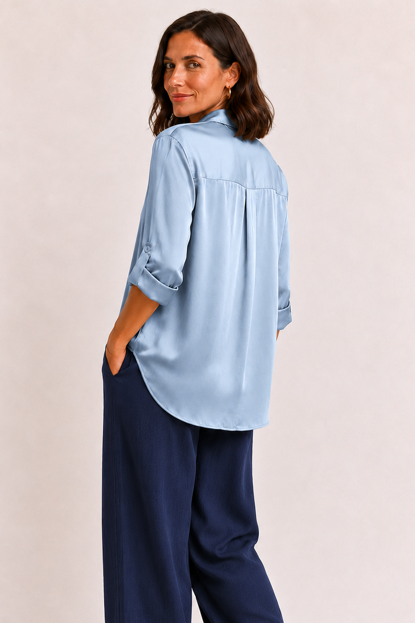 Woman wearing a light blue shirt and navy pants on a beige background