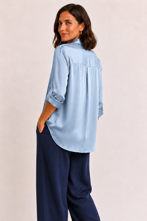 Woman wearing a light blue shirt and navy pants on a beige background