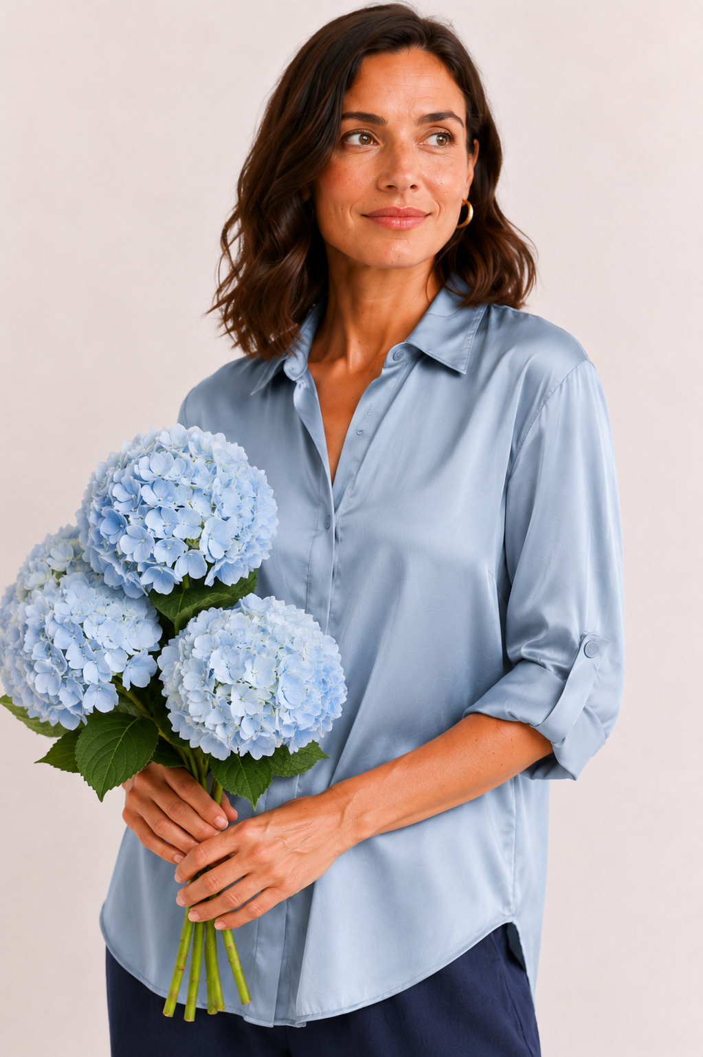 Woman holding a bouquet of blue flowers wearing a light blue shirt against a plain background